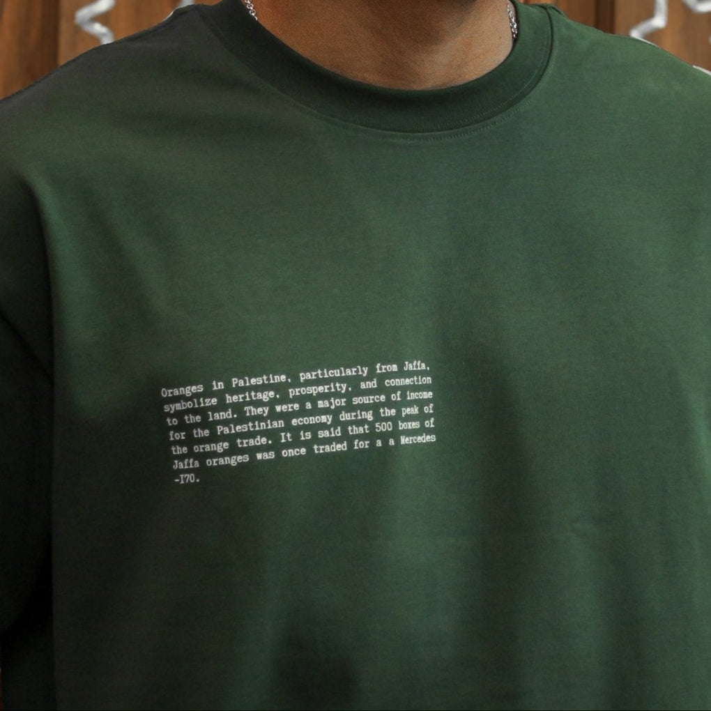 Close-up of the front of the FALASTIN Jaffa Orange T-Shirt in forest color, featuring a text design explaining the historical and cultural significance of Jaffa oranges.