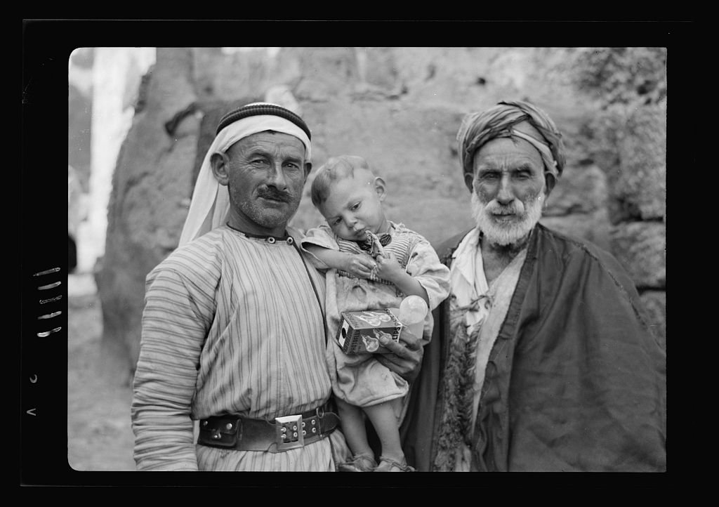 Two Palestinian men photographed at Dhahiriya near Hebron in 1940, the younger in a white hatta held by a black agal over a striped qumbaz with a leather belt, the elder in a wound laffeh turban