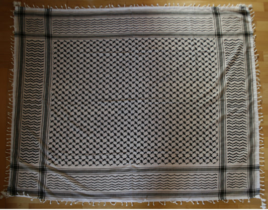 A Palestinian keffiyeh showing the classic black fishnet weave and olive-leaf pattern on white cotton