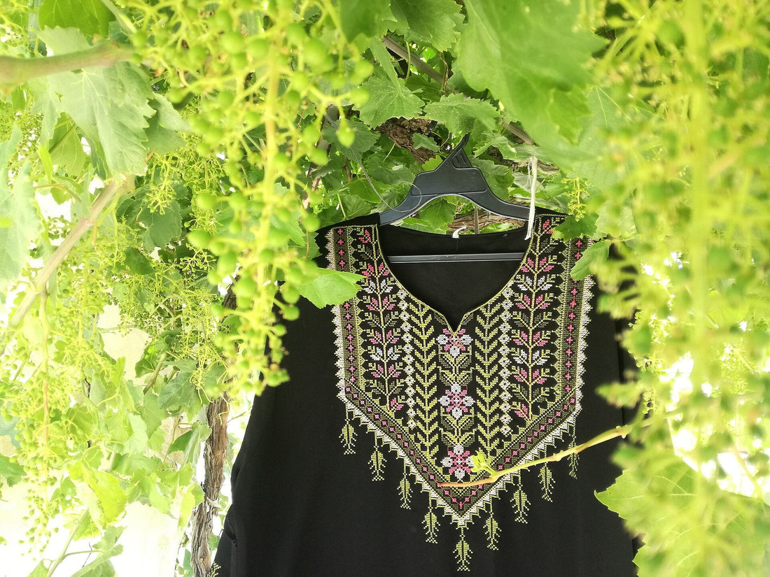 A hand-embroidered Palestinian dress hanging outdoors, its cross-stitch chest panel in red, white and green thread
