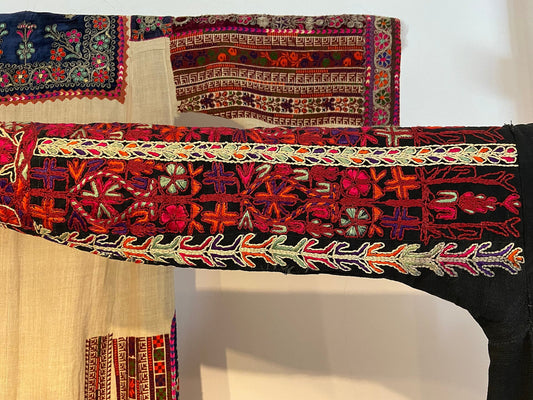 Two embroidered Palestinian dress sleeves displayed side by side, dense geometric cross-stitch in red, orange, purple and gold thread