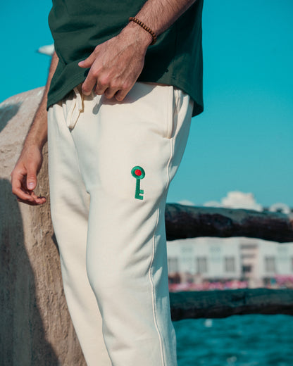Person wearing beige pants with a Palestinian green key design, standing by a body of water.