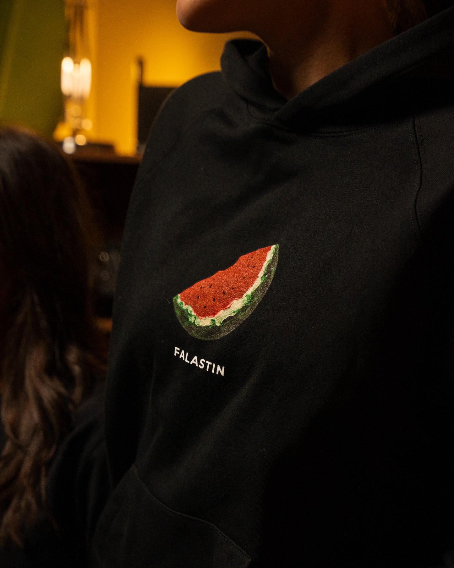 Black hoodie with Palestinian watermelon design and 'FALASTIN' text on a dark background