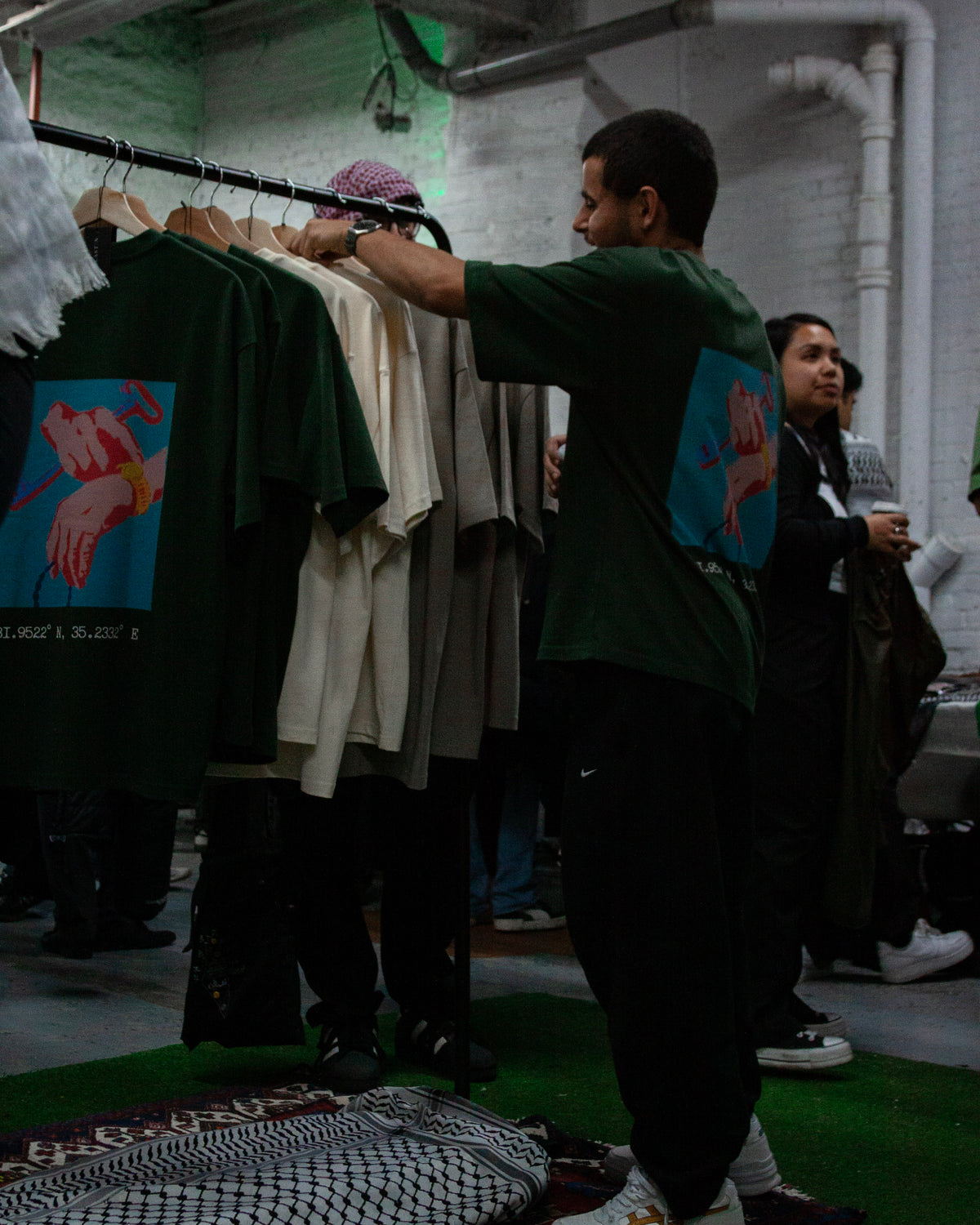 People browsing a rail of FALASTIN t-shirts and keffiyehs at a pop-up