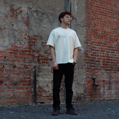 A model wearing the Jaffa Orange T-Shirt in Sand from FALASTIN, featuring front text that highlights the cultural and historical significance of Palestinian oranges. The rich forest green color contrasts beautifully with the rustic brick wall backdrop, emphasizing the deep connection to Palestinian heritage.