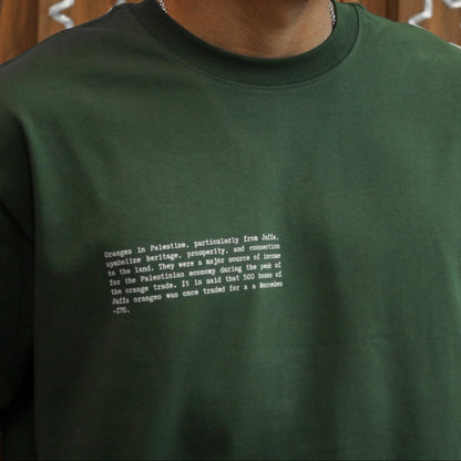Close-up of the front of the FALASTIN Jaffa Orange T-Shirt in forest color, featuring a text design explaining the historical and cultural significance of Jaffa oranges.