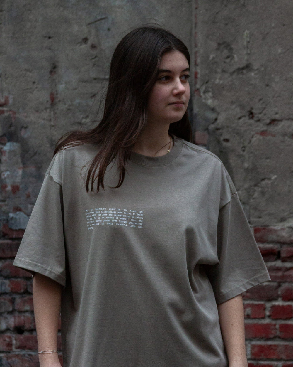 Model wearing the FALASTIN Key T-Shirt in coffee color, featuring a minimalist text design on the front that explains the significance of the key symbol.