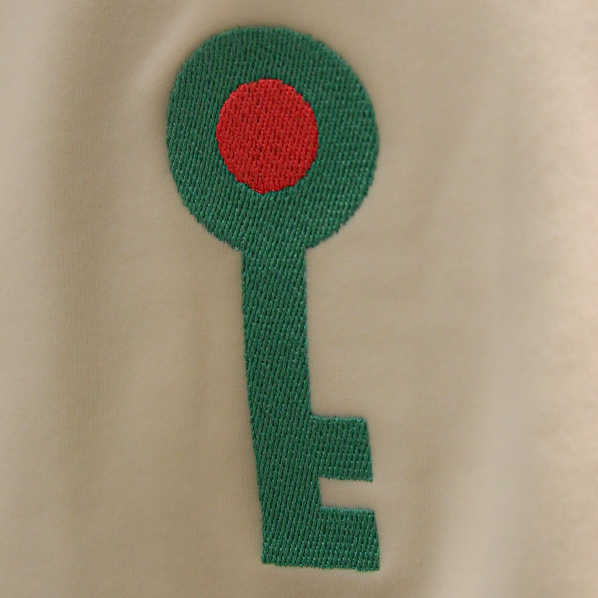 Close-up of a green and red embroidered key logo on a sand-colored hoodie, symbolizing Palestinian heritage and identity.