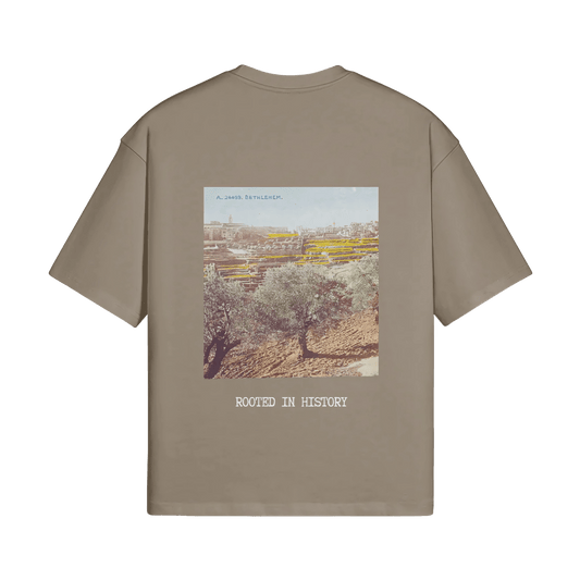 A mockup image of the Heritage Olive Tree T-Shirt from FALASTIN in Coffee
, showcasing the back design featuring a vibrant illustration of a Palestinian olive tree with the words ‘Rooted in History.’ The image is set against a transparent background to highlight the details of the design.