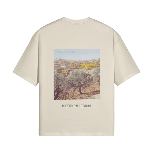 A mockup image of the Heritage Olive Tree T-Shirt in sand from FALASTIN, showcasing the back design featuring a vibrant illustration of a Palestinian olive tree with the words ‘Rooted in History.’ The design is displayed on a transparent background, emphasizing the unique sand color of the t-shirt.