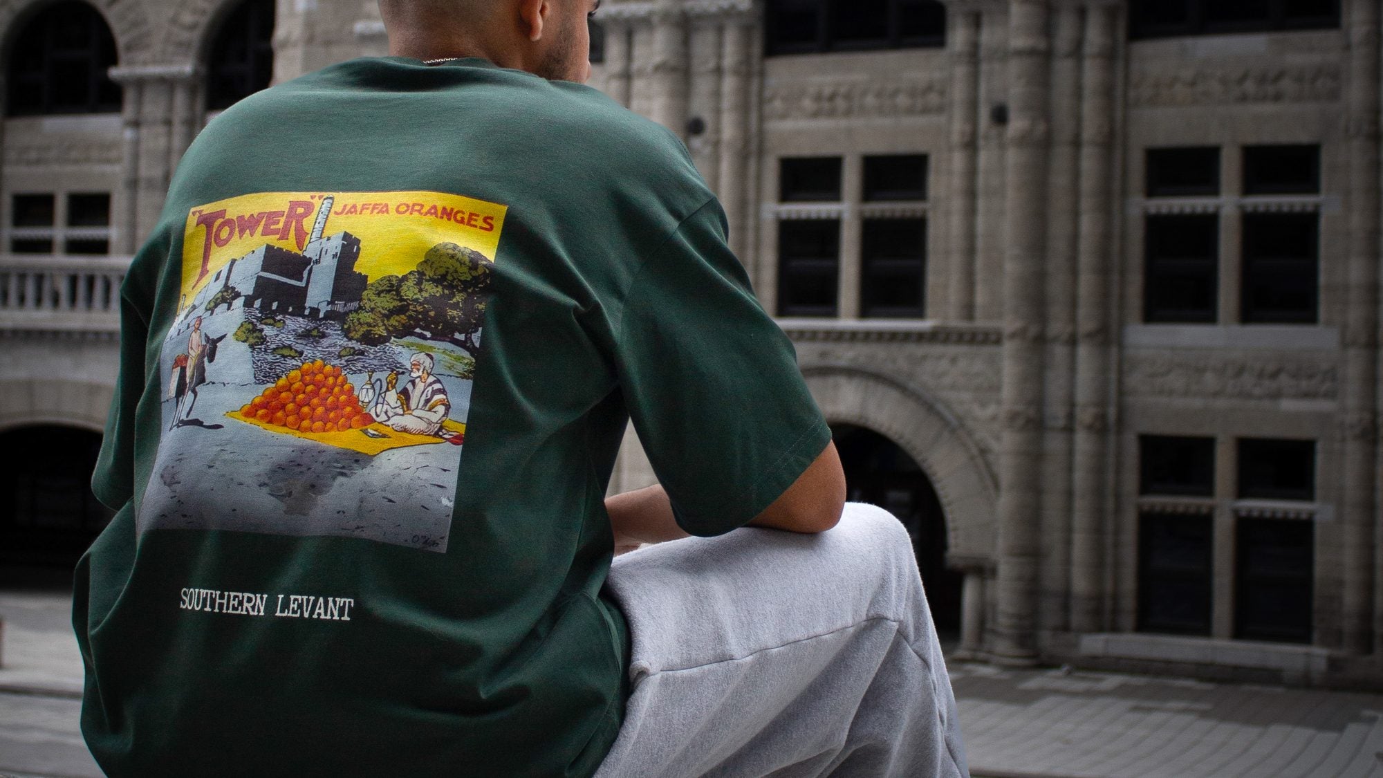 Man wearing the FALASTIN Jaffa Oranges green tee with Southern Levant back print